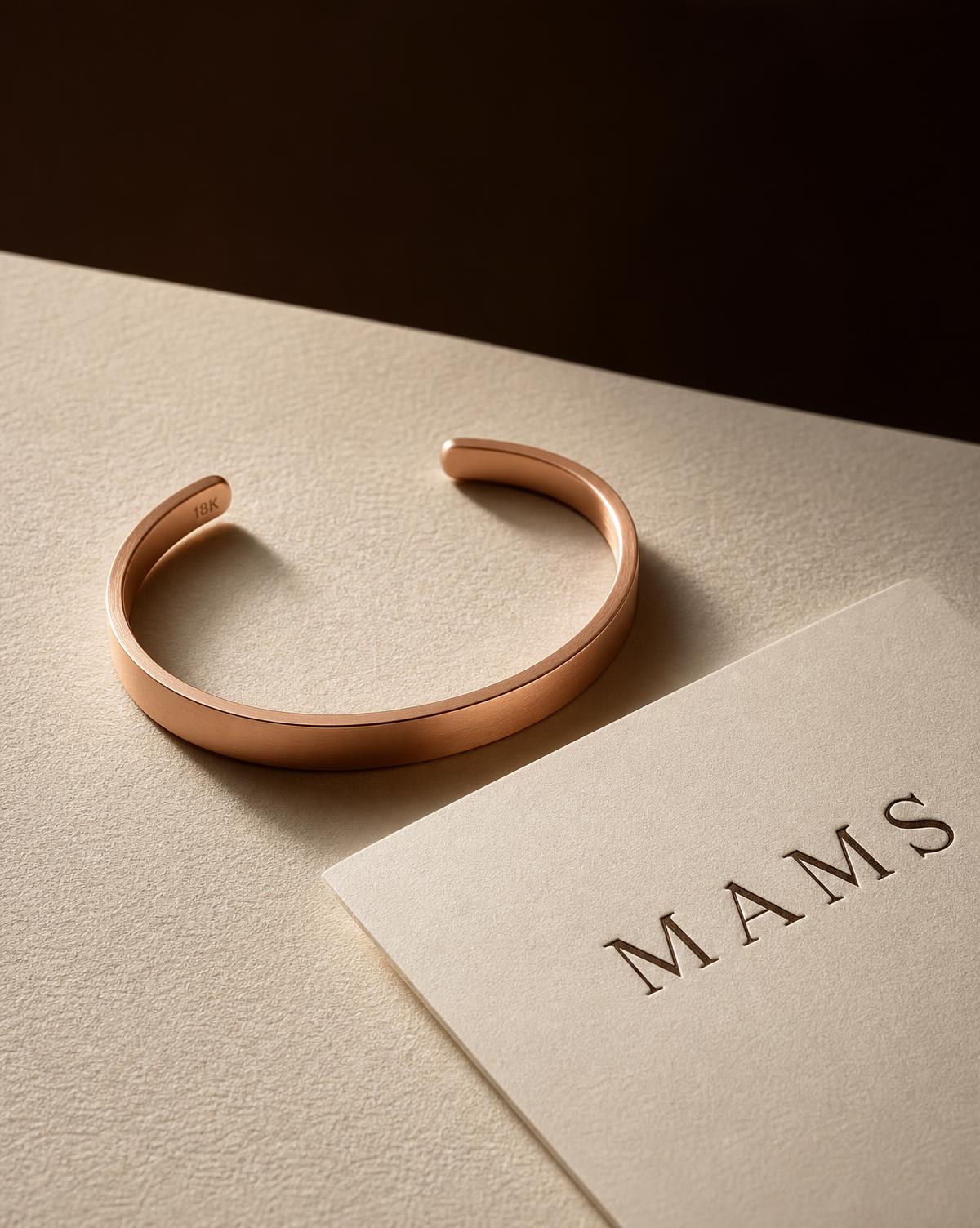 MAMS Quiet Cuff in satin-finished 18K rose gold, standing open on ivory paper